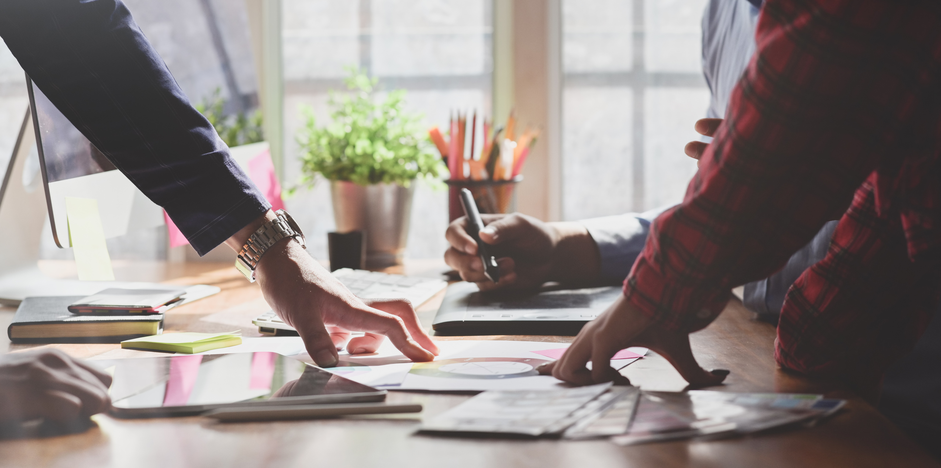 Faceless colleagues working on drawing tab near flyers in office
